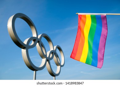 RIO DE JANEIRO - MAY 4, 2016: A Gay Pride Rainbow Flag Hangs In Front Of Olympic Rings Standing Under Bright Blue Sky.