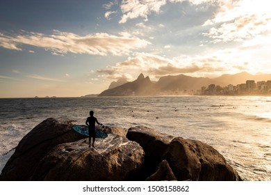 Rio de Janeiro/Rio de Janeiro/Brasil - July, 19 - 2019: Surfer with surfboard in hand watching sunset at Pedra do Arpoador, Arpoador Beach, Rio de Janeiro, Brazil