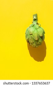 Ripe Artichokes On Solid Yellow Green Background. Hard Light Harsh Shadows. Trendy Funky Minimalist Style. Creative Food Poster Banner. Healthy Plant Based Diet Mediterranean Cuisine. Copy Space