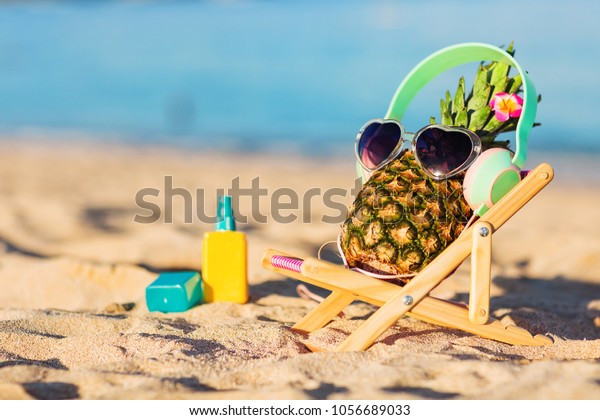 青緑色の海に面した砂の上に スタイリッシュなヘッドフォンを持つ 熟した魅力的なガールパイナップル 音楽を聴いて リラックス サングラスをかけて 熱帯の夏休みのコンセプト 日光浴 の写真素材 今すぐ編集