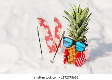 Ripe attractive pineapple in stylish mirrored sunglasses on the snow in the mountain. Winter ski holidays concept. Wearing stylish mittens, sunglass. Sunny day in the mountain. Mountain skiing outfit
