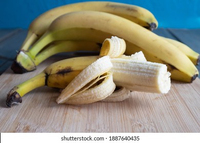 a ripe and bitten banana lies on a wooden board, other bananas lie behind, on the table