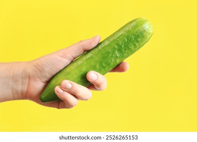 Ripe cucumber in a female hand on a yellow background. Close-up on a hand with a cucumber. Harvest. The concept of healthy eating and diet. Vegetables. White female hand shows a fresh tasty cucumber - Powered by Shutterstock