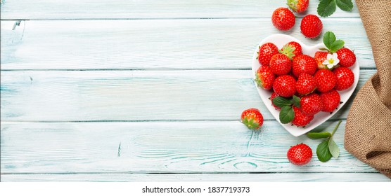 Ripe garden strawberry in heart shaped bowl on wooden table. Top view flat lay with copy space