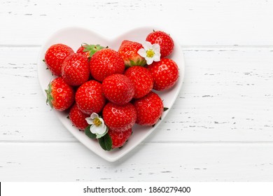 Ripe garden strawberry in heart shaped bowl on wooden table. Top view flat lay with copy space