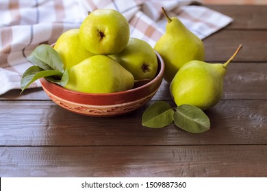ripe green pears in a bowl on a wooden background. fresh pear closeup. background with yellow-green pears and leaves.