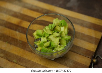 Ripe Juicy Diced Avacado In A Transparent Bowl On A Wooden Cutting Board.