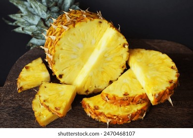 Ripe juicy pineapple next to cut pieces on a wooden board on a dark background - Powered by Shutterstock