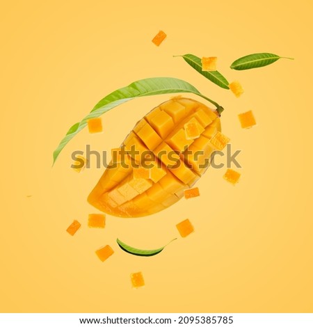 Ripe mango fruit sliced with cube and green leaves floating on yellow background.