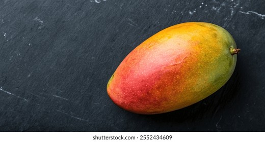 A ripe mango sits on a black surface. The fruit is bright orange and green, and it is fresh and ready to eat - Powered by Shutterstock