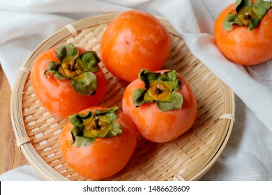 Спелые апельсиновые фрукты хурмы. Свежая хурма на бамбуковой корзине. Плоды хурмы на белой ткани и деревянном столе.