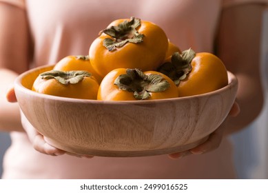 Ripe persimmon fruit in wooden bowl holding by womand hand