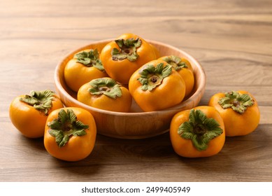 Ripe persimmon fruit in wooden bowl on wooden background