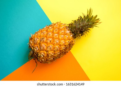 Ripe pineapple on a geometric pattern yellow, ornage and cyan colour background. Flat lay