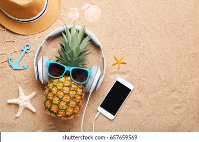 Ripe pineapple with sunglasses and headphones on beach sand - Powered by Shutterstock