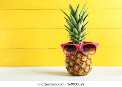 Ripe pineapple with sunglasses on a white wooden table