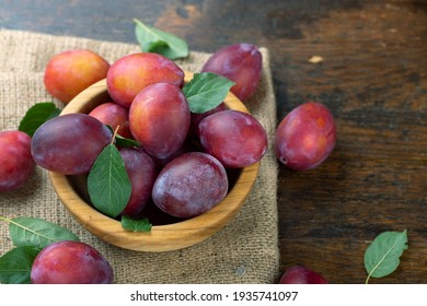 Ripe plums and leaves in a wooden bowl on the table. Harvesting season.