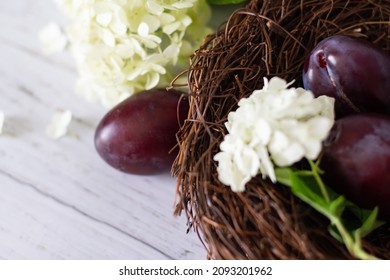 Ripe Plums In A Vine Basket On A Wooden Background, Hydrangea Flowers Lie Nearby