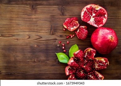 Ripe pomegranate fruit near leaf on dark wooden background top-down copy space