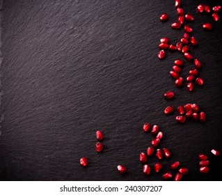 Ripe pomegranate seeds on rough black slate background. Copy space.