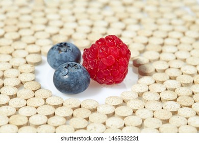 Ripe Raspberries And Blueberries Are Surrounded By Pills On All Sides. Concept: Natural Vitamins. Close Up.