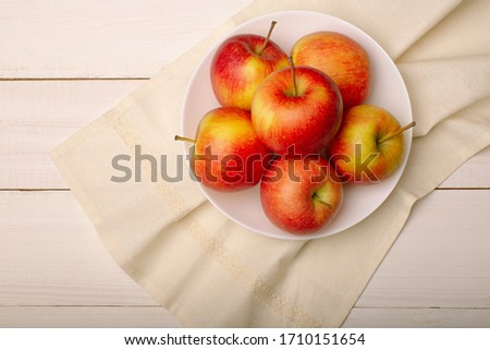 Ripe red apples in a bowl on white wooden table, top view.