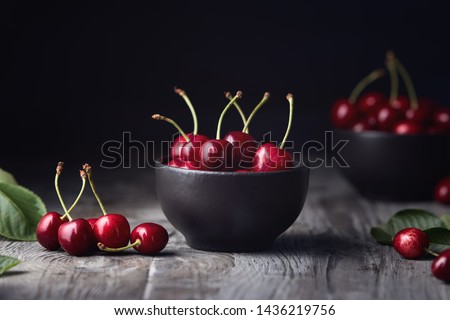 Ripe red cherries in a bowl and next to it on wooden table.