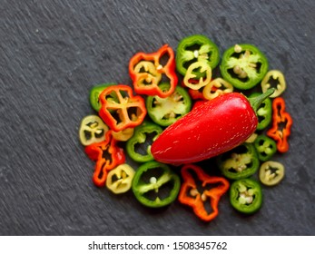 Ripe Red Jalapeno Pepper On A Blurred Background Of Chopped Rings Of Peppers And Black Stone. Selective Focus, Top View.