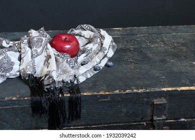 Ripe red macintosh apple positioned on black and white chiffon scarf placed on surface of old wooden vintage trunk