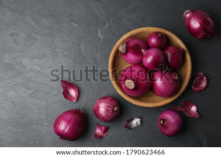 Ripe red onion bulbs and bowl on black table, flat lay. Space for text