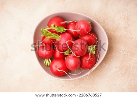 Ripe red radish in a bowl on a beige background, closeup. Fresh red radish.