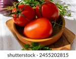 Ripe red Roma tomatoes in bowl with fresh herbs on table