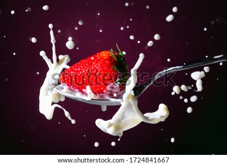 Ripe red strawberry falls into a spoon of milk in front of a black background - Splash