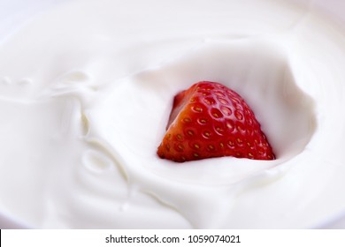 Ripe red strawberry splashing into fresh creamy white yogurt