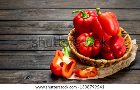Ripe red sweet peppers in a basket on paper. On wooden background