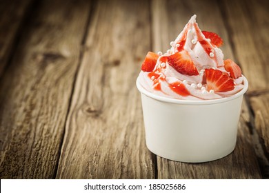 Ripe red tropical strawberries and vanilla ice frozen joghurt cream for a healthy refreshing cold summer dessert in a takeaway tub on an old rustic wooden table with copyspace