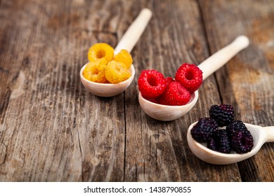 Ripe red and yellow raspberries and blackberries in spoons on an old wooden table. Delicious berries. - Shutterstock ID 1438790855