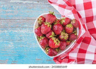 Ripe strawberries in a white bowl heart shaped and checkered napkin on a old blue paint wooden background - Powered by Shutterstock