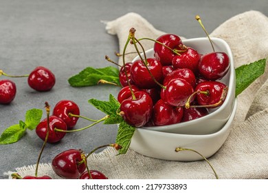 Ripe sweet cherries with fresh mint leaves, traditional summer fruits. Trendy beton stands, vintage napkin. Grey stone concrete background, close up