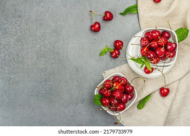 Ripe sweet cherries with fresh mint leaves, traditional summer fruits. Trendy beton stands, vintage napkin. Grey stone concrete background, top view