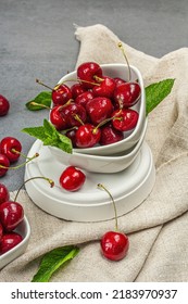 Ripe sweet cherries with fresh mint leaves, traditional summer fruits. Trendy beton stands, vintage napkin. Grey stone concrete background, close up
