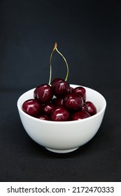 Ripe sweet cherries in a white bowl. Grey background.