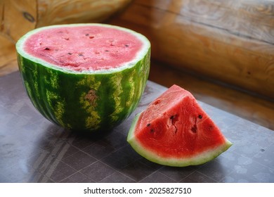 A ripe watermelon with a part cut off from it lies on the table against the background of a log wall. close-up. Green watermelon with red juicy pulp and dark grains. Watermelon season, natural photo. 