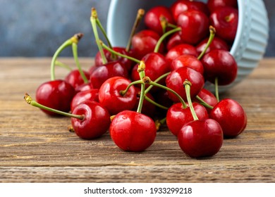 Ripe wet sweet cherries are poured out of the blue bowl on wooden background