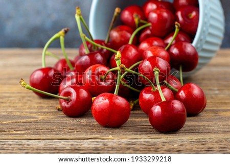Ripe wet sweet cherries are poured out of the blue bowl on wooden background