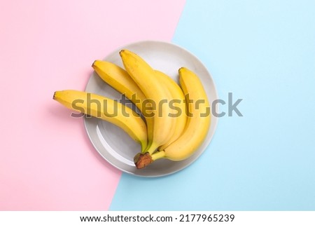 Ripe yellow bananas on plate, blue-pink pastel background. Top view
