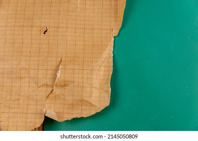 Ripped Crumpled Sheet Of Millimeter Graph Paper Against A Green Background. Brown Paper For Drafting, Design, Engineering, And More. Abstract Multitasking Background.