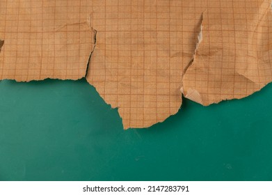 Ripped Crumpled Sheet Of Millimeter Graph Paper Against A Green Background. Brown Paper For Drafting, Design, Engineering, And More. Abstract Multitasking Background.