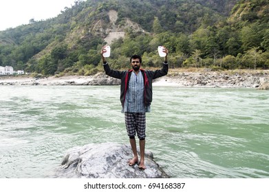 RISHIKESH, INDIA - JANUARY 16, 2017: a man showing the bottle of holy water in both hands on the riverbank of ganges river 