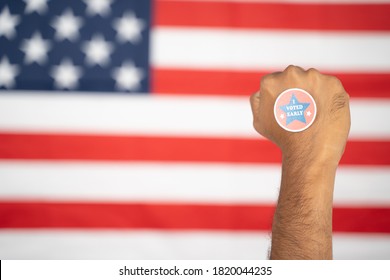 Rising Fist With I Voted Early Sticker On Hand With US Flag As Background - Concept Of Early Voting At US Election.